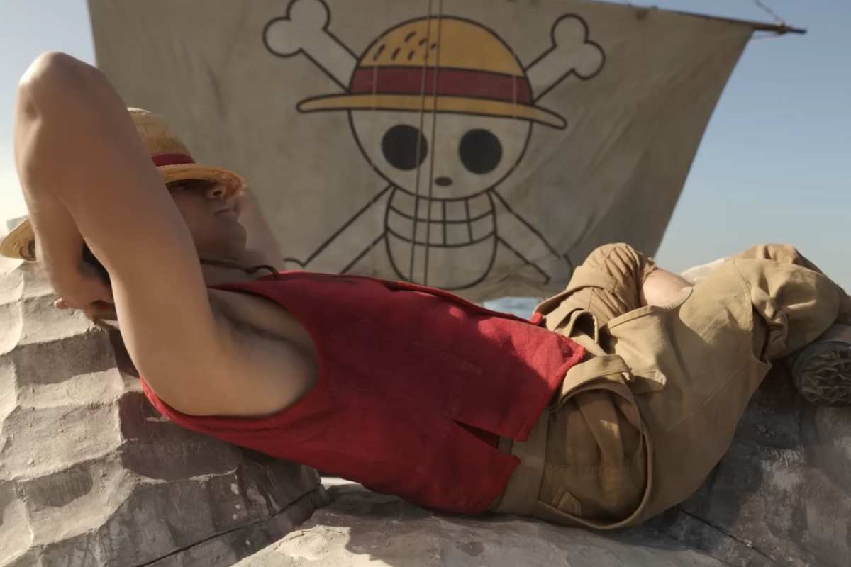 Il personaggio di One Piece Monkey D. Rufy sdraiato su un lato con alle spalle la bandiera dei pirati suo simbolo con un teschio ed un cappello in testa