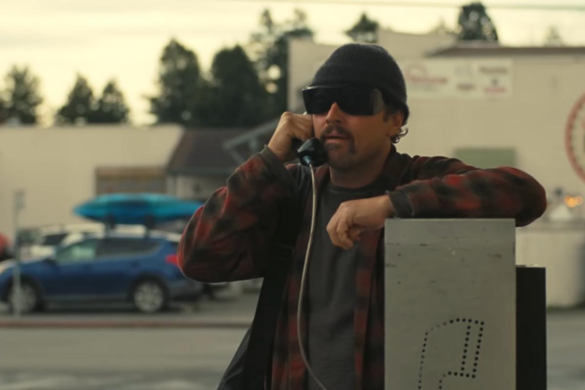 Leonardo DiCaprio con berretto e camicia scozzese al telefono in una scena del film One Battle After Another