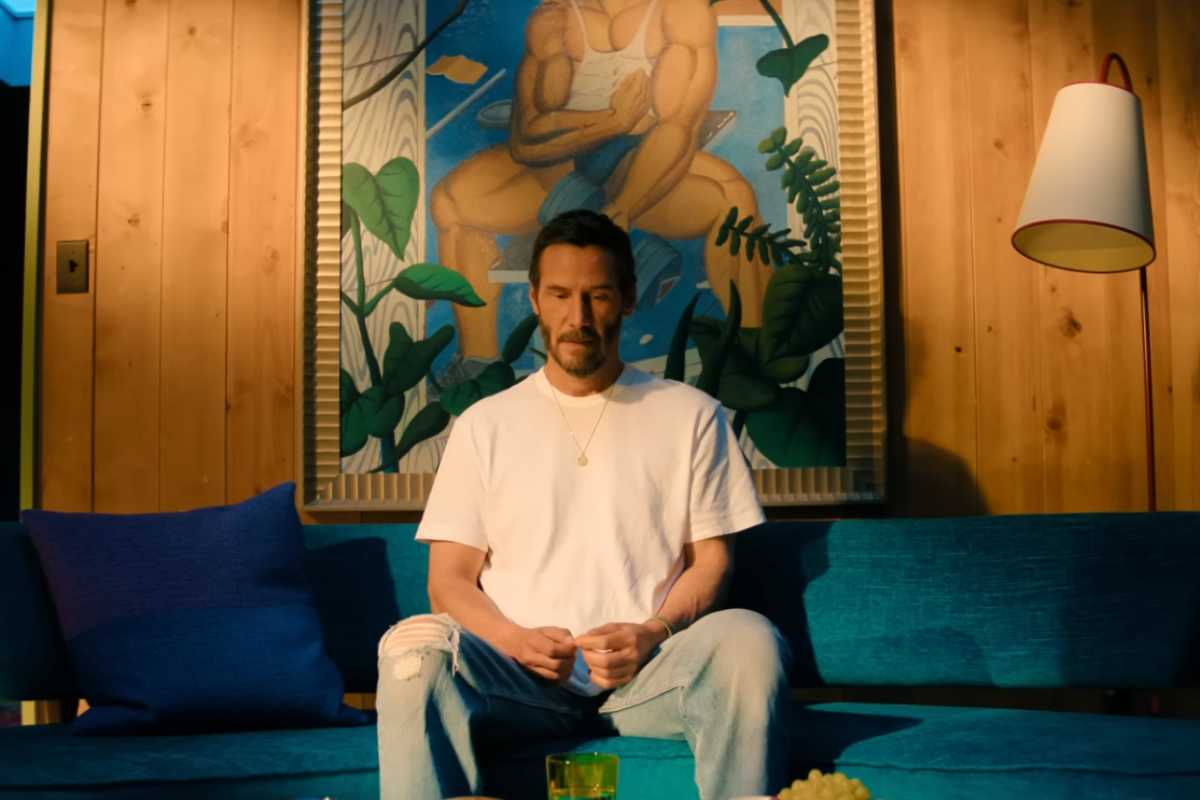 Keanu Reeves seduto su un divano con il capo chinato in una scena di Outcome
