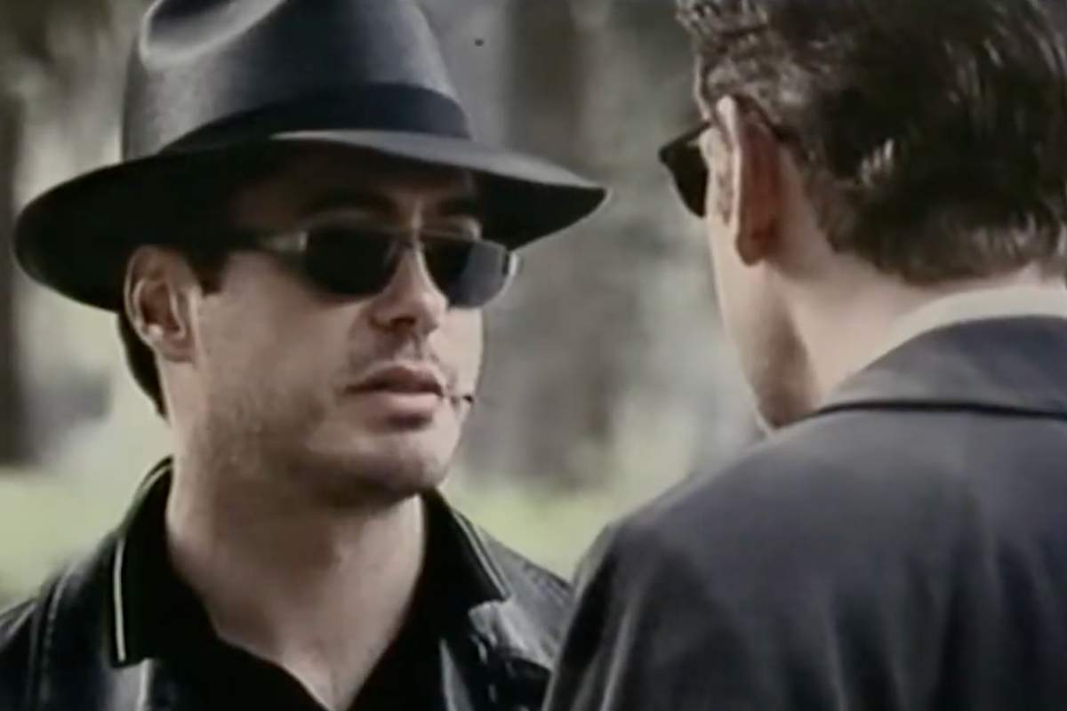 Robert Downey Jr. in una scena di Conflitto di interessi: cappello borsalino in testa e occhiali da sole parla con qualcuno che vediamo di spalle