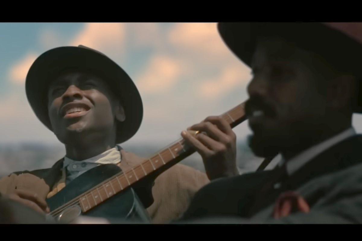 Un uomo afroamericano suona la chitarra in macchina in una scena del film Sinners