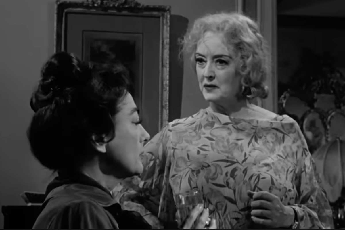Joan Crawford in primo piano in sedia a rotelle dietro Bette Davis in piedi