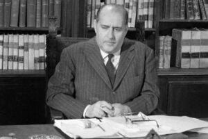 Roberto Rossellini seduto alla scrivania con alle spalle una libreria