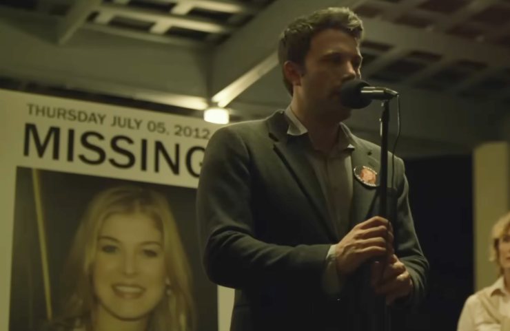 Ben Affleck con davanti un microfono e dietro di se la foto di Rosamund Pike