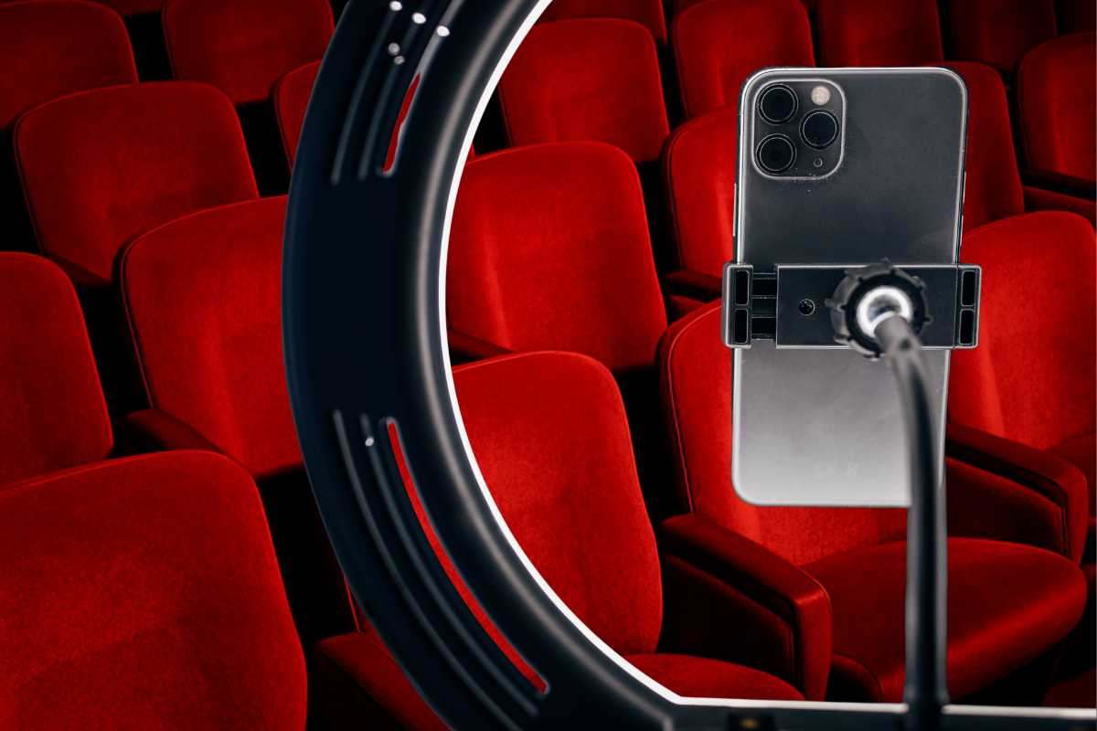Cellulare posizionato su treppiede e sullo sfondo le poltrone del cinema